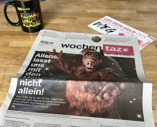 Die wochentaz mit Alf auf dem Titel „Aliens, lasst uns mit den Menschen nicht allein!“. Dahinter steht der Frühstückskaffee in der Tasse des tazlab 2022 Klima und Klasse!