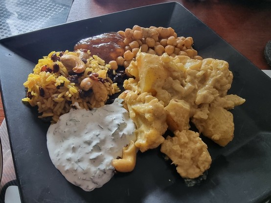 Man sieht einen Teller mit unterschiedlichen nordindischen und persischen Speisen, unter anderem Kartoffeln, Blumenkohl, Reis und Kichererbsen.