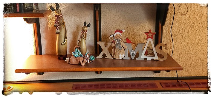 Foto eines Regals im Wohnzimmer mit Weihnachtsdekoration. Zwei Elche und ein XMas Schriftzug aus Holz.