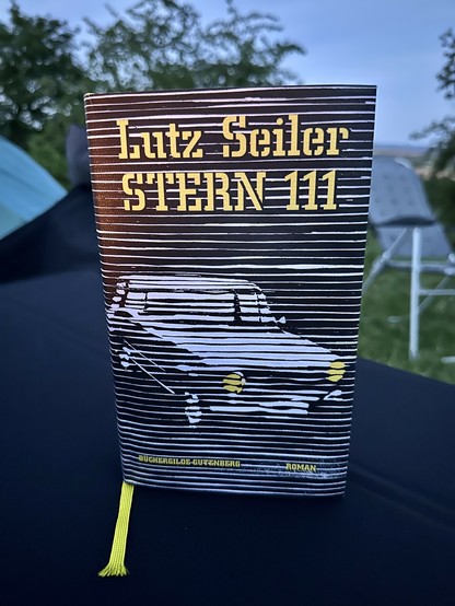 Auf dem Campingtisch im Kerzenschein steht der Roman Stern 111 von Lutz Seiler, es ist die Hardcoverausgabe der Büchergilde, gestaltet von Franziska Neubert. 