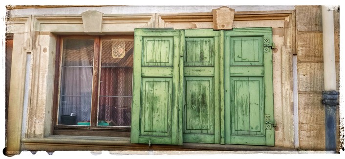 Aufnahme zweier Sprossen-Fenster mit grünen Fensterläden. Die Läden des rechten Fensters sind geschlossen, die des linken Fensters sind offen. Die Fenster sind in Sandstein eingefasst. Hinter den Scheiben sieht man Gardinen.
