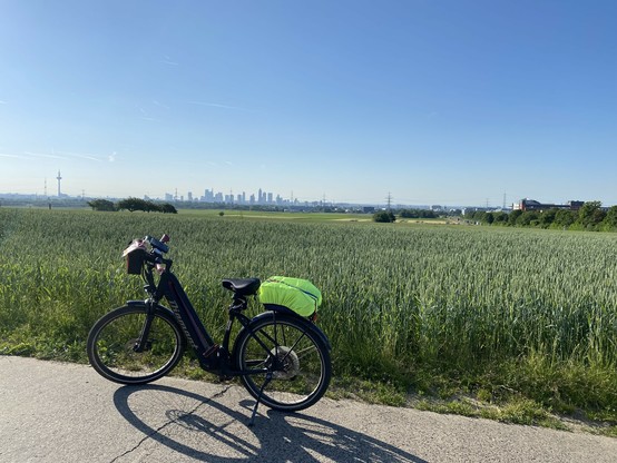 Fahrrad steht auf einem Feldweg, in der Ferne die Hochhäuser von Frankfurt, der Himmel ist strahlendblau