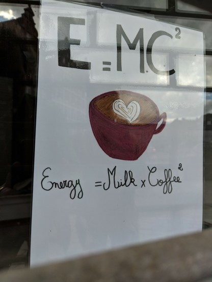 ein handgemaltes Schild mit einer Tasse mit Schaum in Herzform drin. Drüber steht groß:  E=MC2. Drunter steht: Energy = Milk * Coffee2