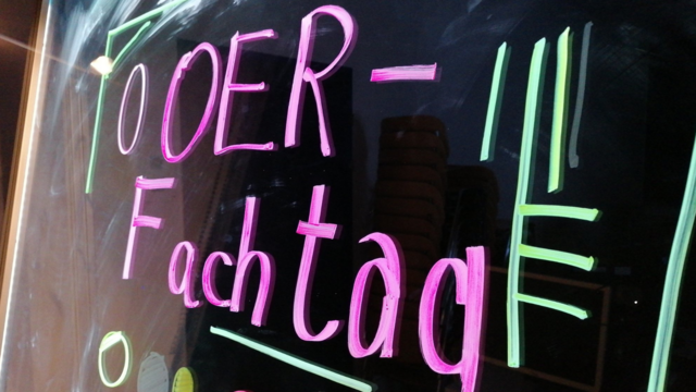 Der Schriftzug OER-Fachtag in Neonfarben auf einer Glasoberfläche.