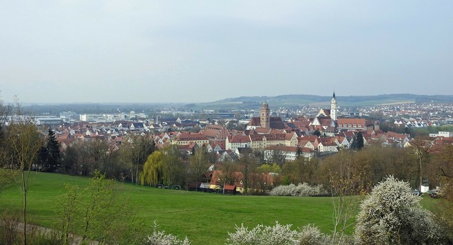 Panorama der gesuchten Stadt von einer Anhöhe im Nordosten aus gesehen. Zwei Kirchtürme ragen empor. Der dunklere Turm gehört zum Liebfrauenmünster. Der schlanke helle Turm ist Teil der Klosterkirche Heilig Kreuz.