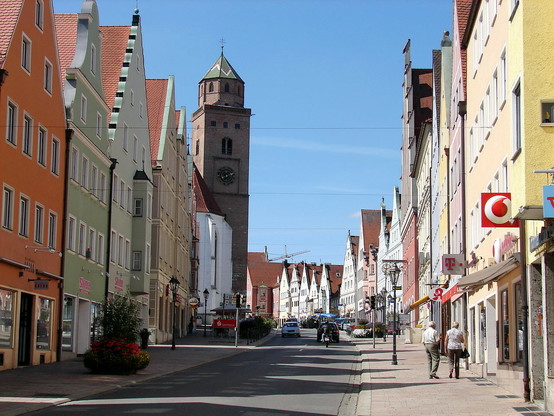 Das Bild zeigt die Reichsstraße in der gesuchten Stadt, die rechts und links von eindrucksvollen Häuserfassaden gesäumt wird. Links steht das Liebfrauenmünster.