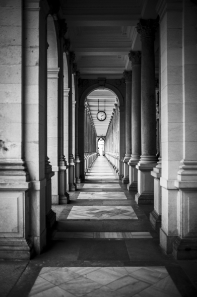Das Foto zeigt einen Blick in einen Säulengang der so genannten Mühlbrunnkolonnade. Säulen reihen sich symmetrisch in einer Flucht, scheinbar in die Unendlichkeit. 