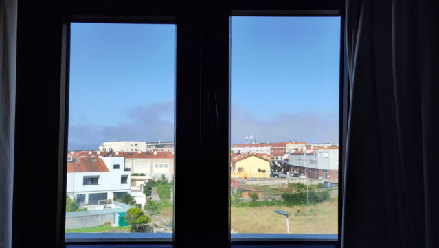 Ein Blick aus einem Fenster. Er fällt auf eine portugiesische Kleinstadt mit weißen und gelben Häusern und roten Dächern. Der Himmel ist blau.