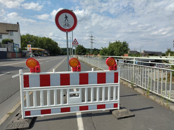 Ein Geh- und Radweg ist durch eine rot-weiße Absperrung gesperrt. Ein Schild weist darauf hin, dass die Nutzung des Weges für Radfahrende und zu Fuß Gehende verboten ist.