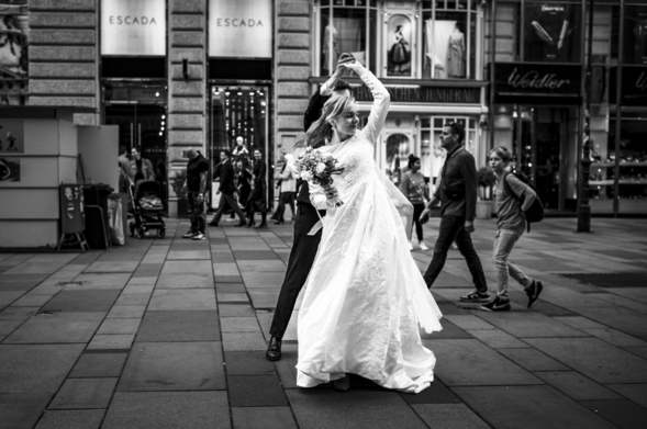 In schwarz-weiß: Ein tanzendes Hochzeitspaar, mitten auf einer Einkaufsstraße in Wien. Passanten gehen im Hintergrund vorbei.