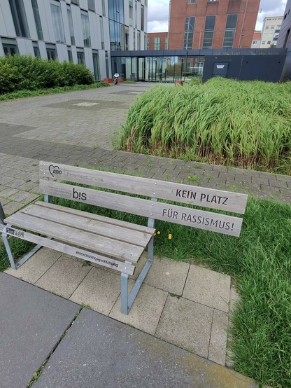 Parkbank an der Aussenweser in Bremerhaven mit der Aufschrift „KEIN PLATZ FÜR RASSISMUS!“ Das Stück Holz darunter fehlt.

#BREMERHAVENgegen RASSISMUS