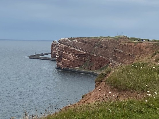 Blick auf die Steilküste von Helgoland. Die Felsen sind rot-weiss gestreift.  