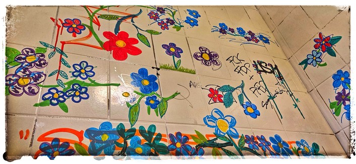 Ausschnitt einer mit weißen Kacheln gefliesten Wand, auf die bunte Blumen gemalt wurden.