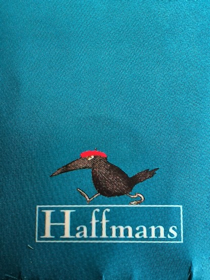 Detail eines Buchrückens. Auf blauem Hintergrund der Schriftzug Haffmanns in dünnem Rahmen, auf dem ein komplizenhafter Rabenvogel mit roter Baskenmütze nach links läuft. 