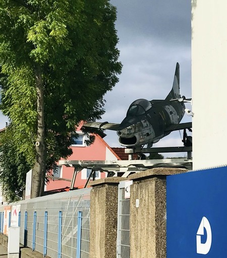 Ein kleines, gammeliges Flugzeug steht rechts oben neben der Straße, zielt nach schräg unten