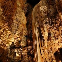 Eine Höhle voller Stalaktiten, manche tropfenformug, andere flächig (wie Elefantenohren). Die Höhle ist in einem schummerigen orangenes Licht getaucht