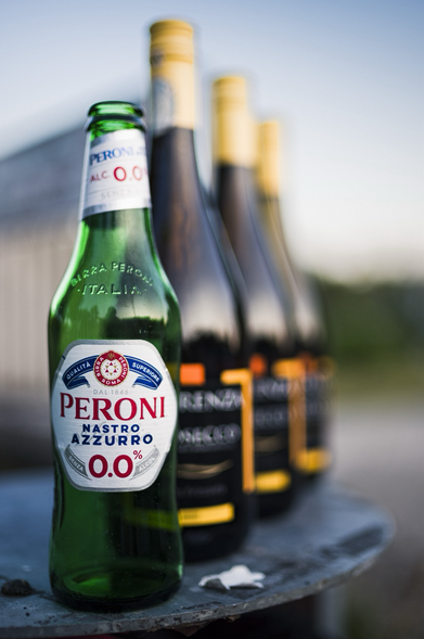 Aufgereiht hintereinander stehen mehrere leere Flaschen. Im Vordergrund, eine grüne Flasche mit dem Aufdruck: Peroni, Nastro Azzurro, 0,0%