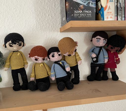 Häkel Crew der Enterprise im Regal. Von links nach rechts: Sulu, sitzend Chekov, sitzend Spock, Kirk schaut nach unten, Scottys Lücke, Bones und Uhura, die wie Kirk nach unten schaut 