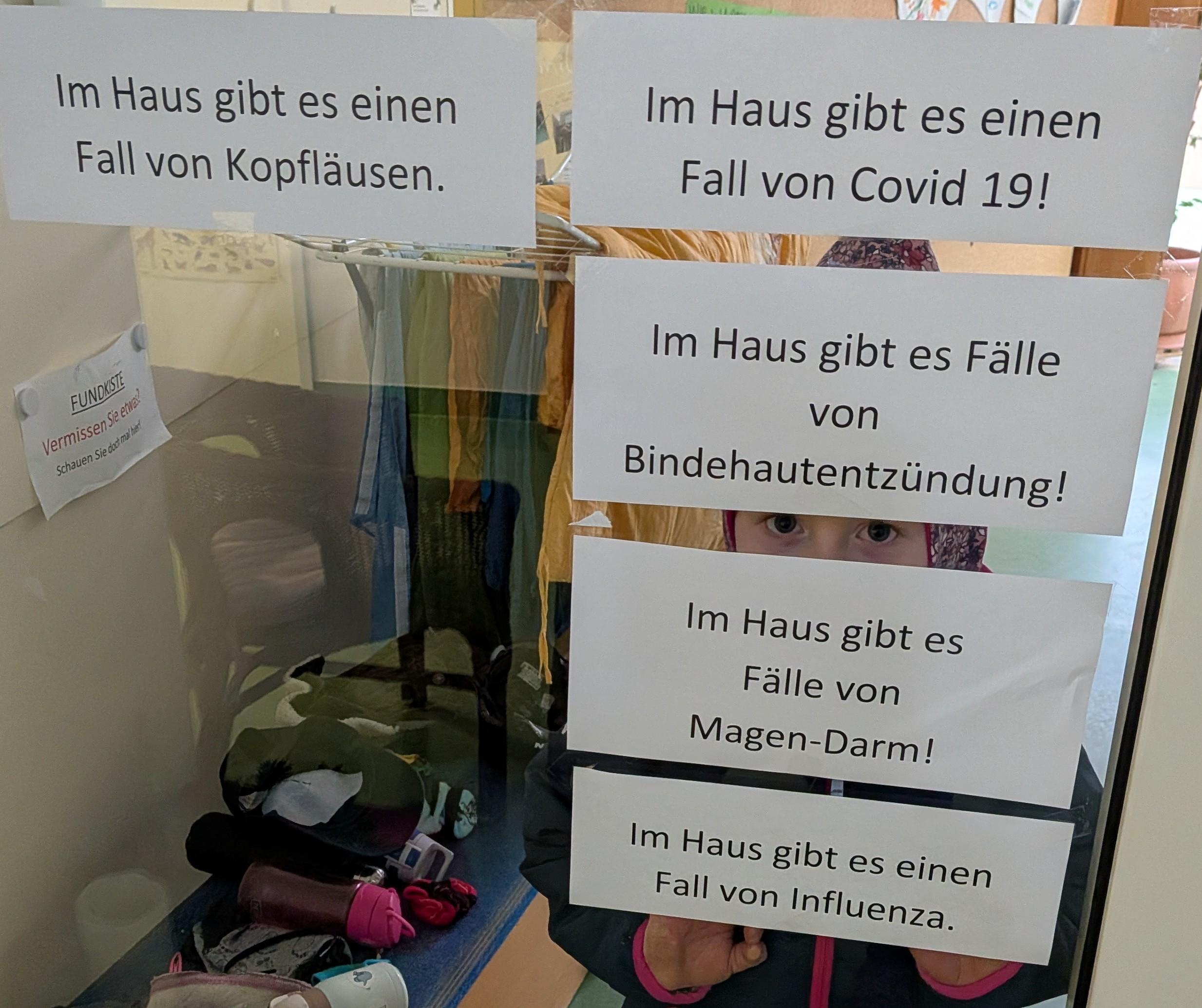 5 Zettel mit den Aufschriften Im Haus gibt es Fälle von Covid 19, Bindehautentzündung, Magen-Darm, Kopfläusen und Influenza