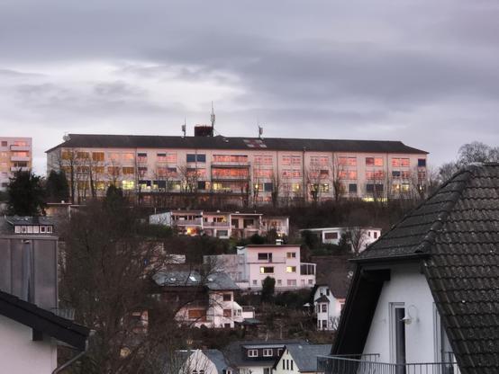 Morgenröte gespiegelt in den Fenstern des ehemaligen Krankenhauses in Bad Schwalbach. Auf dem Dach ist ein rotes Kreuz gemalt für Rettungshubschrauber. Krankenhaus ganz oben, Wohnhäuser am Hang. 