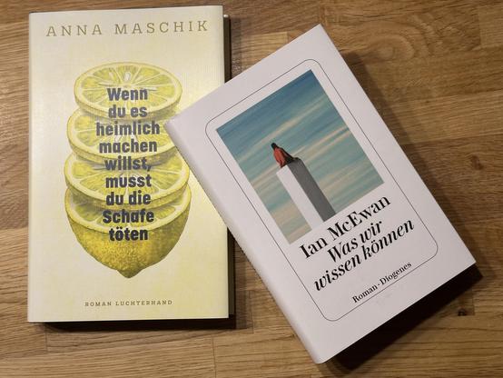 Auf dem Bild liegen zwei Bücher auf einem Holztisch:
- Links das Buch "Wenn du es heimlich machen willst, musst du die Schafe töten" von Anna Maschik mit einem Cover, das Zitronenscheiben zeigt.
- Rechts der Roman "Was wir wissen können" von Ian McEwan mit einem Cover, das eine Person auf einem schmalen Turm vor blauem Himmel abbildet.