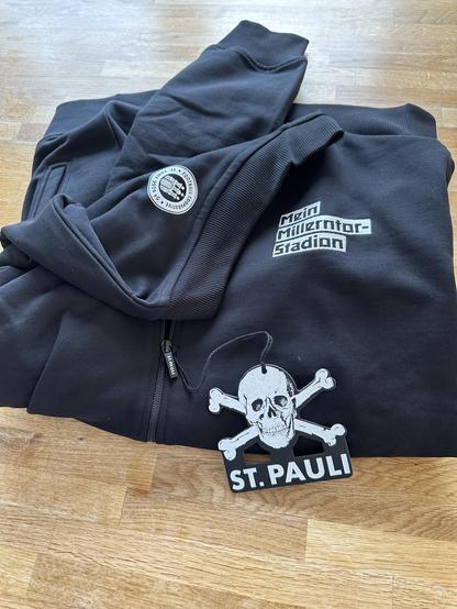 Collegejacke „Mein Millerntorstadion“ der Football Cooperative St. Pauli 2024 eG mit einem typischen Totenkopf Anhänger. 