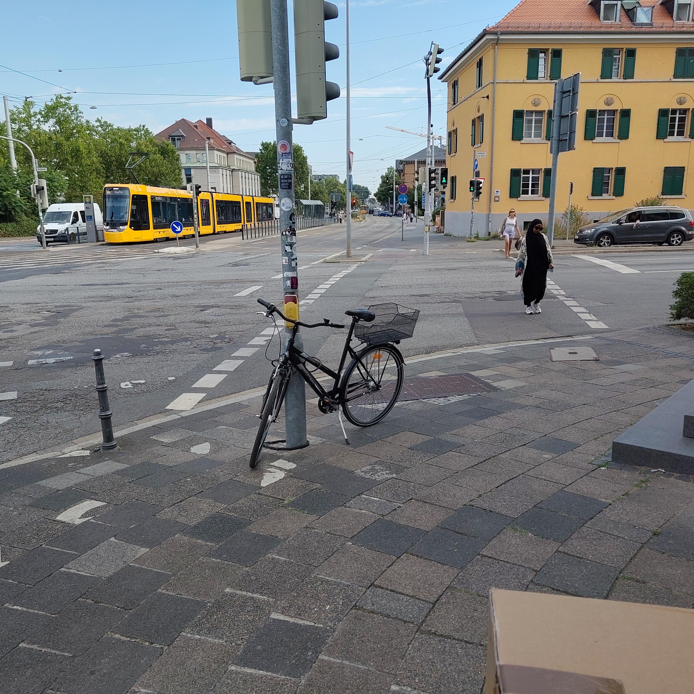 Fahrrad an einer Ampel angeschlossen, Lenker behindert den Zugang zum Druecker.