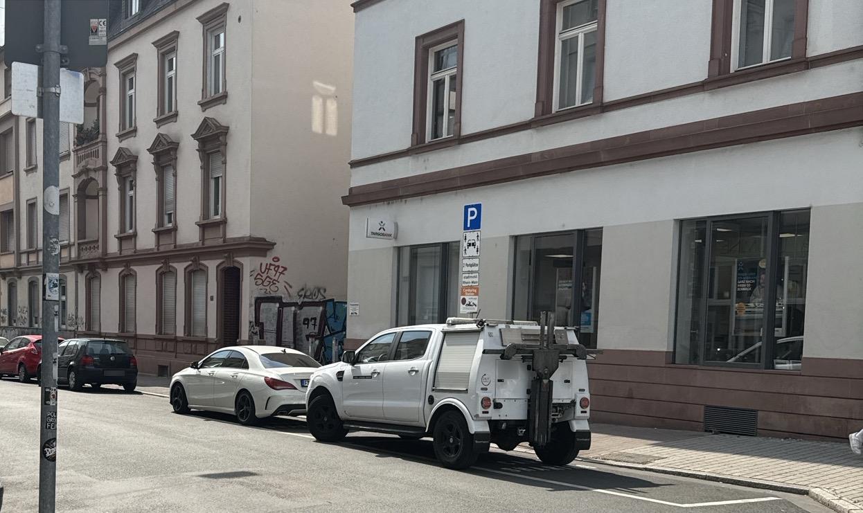 2 Carsharing-Parkplätze auf der Fahrbahn. Vorne ein weißer Mercedes, auf dem zweiten Parkplatz direkt dahinter ein Abschleppwagen