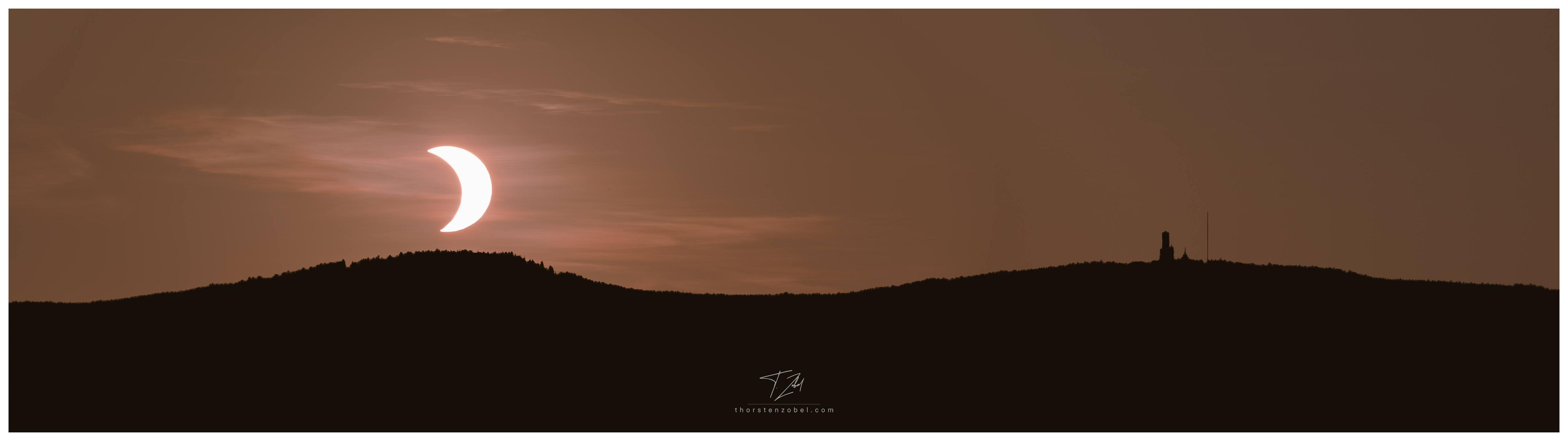 Above the black silhouette of a mountain range, the sun appears as a crescent. The effect is caused by a partial solar eclipse.