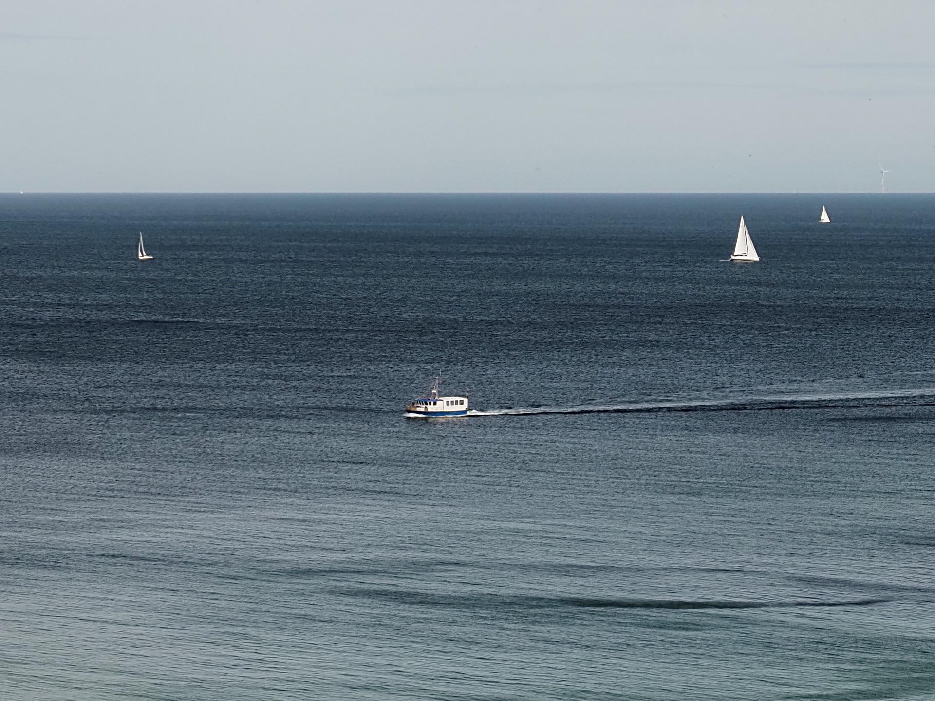 Farbiges Querformat. Es sind auf blauem Meer mit kleinen Wellen vier Boote zu sehen.